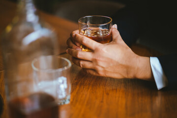 A stylish man holds a glass of whiskey in a fancy pub amidst a crowd of celebrants. The warm and elegant atmosphere accentuates the rich amber-colored liquid.