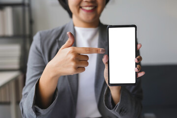Businesswoman is smiling and pointing at a smartphone with a blank screen, perfect for your advertisement