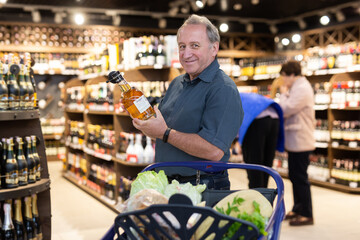 Mature man choosing nice bottle of liquor in supermarket