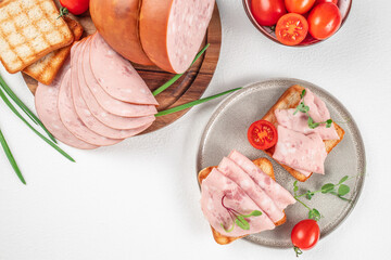 Plate of tasty sandwiches with boiled sausage and tomato on white table