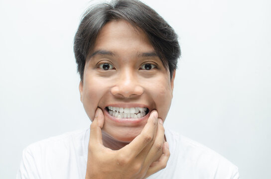 young asian man smiling and showing his crooked teeth isolated over white background. dracula teeth and bucktooth concept. overlapping teeth of man