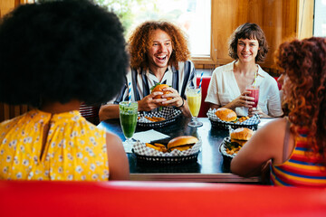 Multiethnic group of friends having meal at 80s vintage diner restaurant - Multiracial young people bonding and having fun, eating in an american fast food burger house