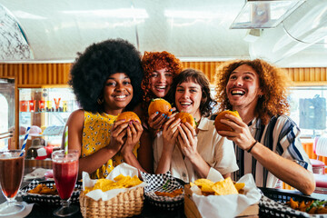Multiethnic group of friends having meal at 80s vintage diner restaurant - Multiracial young people bonding and having fun, eating in an american fast food burger house
