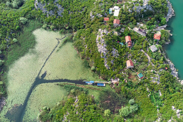 Aerial view of Lake Skadar, Montenegro, featuring a fishing village nestled in the valley, surrounded by majestic landscapes and vibrant duckweed.