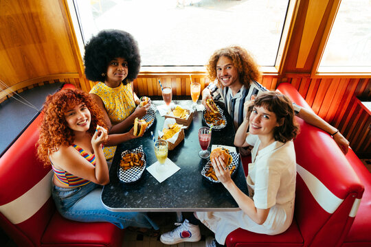 Multiethnic group of friends having meal at 80s vintage diner restaurant - Multiracial young people bonding and having fun, eating in an american fast food burger house