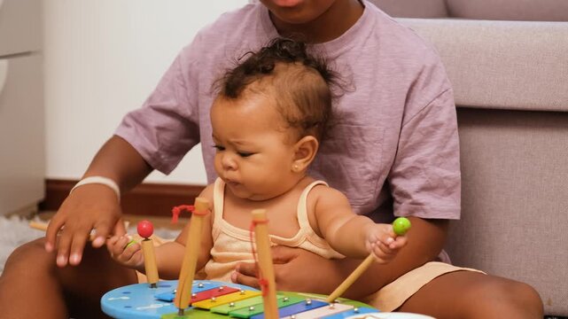 Older brother is bonding with his baby sister while playing a toy xylophone