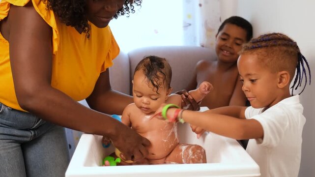 Mother is giving a bath to her baby girl while her sons watch and help