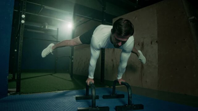 Athletic man with strong muscular arms and body performing advanced straddle planche while training at dark loft style gym