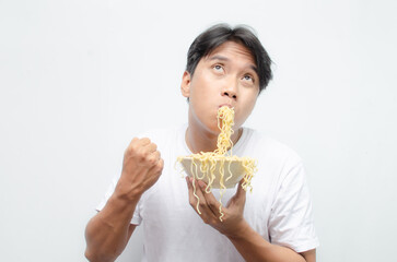 young asian man eats noodles. ecstatic young asian man with mouth full of noodles. young man in white tshirt enjoying noodles.
