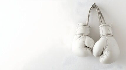 A pair of pristine white boxing gloves hanging from a hook against a plain white wall leaving ample copy space at the bottom for text overlay  The gloves symbolize the sport of boxing fitness