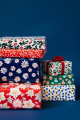 Obraz premium stack of festive Christmas presents wrapping paper has retro poinsettia prints in white blue red and gold silver colors, dark blue background