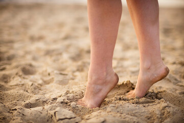 Fototapeta na wymiar Feet on the sand. Sea. Beach. Summer. Seashore. Riverbank. Slender tanned legs