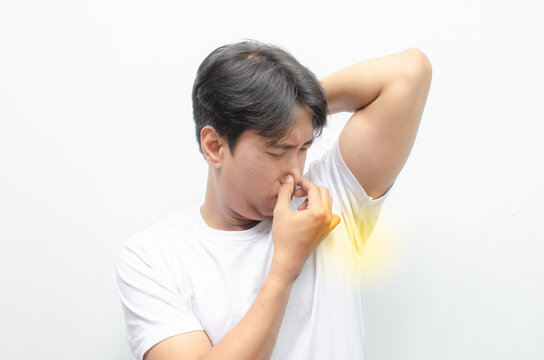 young sian man in white t-shirt smells his bad odor armpit isolated on white background. asian man feels embarrassed because his arm pit emitting bad odor and yellow stain on his tshirt.