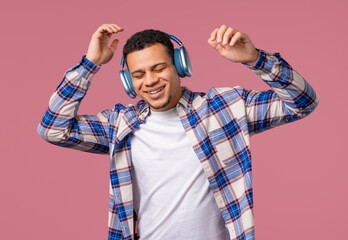 Happy positive man listening music, enjoying dance with headphones, pink studio