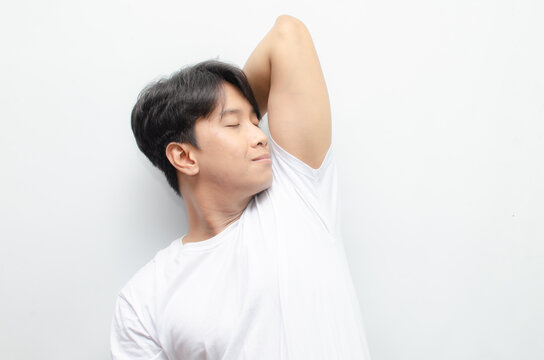 A young Asian man in white tshirt smells the freshness of his odor from armpit. Man enjoys his freshness and cleanliness. man smelling his armpit