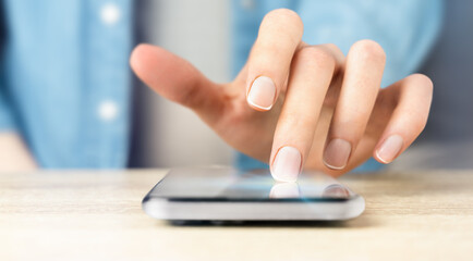female hand pressing on smartphone screen lying on table, close-up