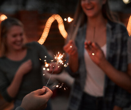 Hands, sparkle and people with glow outdoor for celebration, light and success of new years party. Happy, friends and fireworks with flame shine, announcement and achievement memory at night together