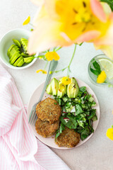 Quinoa cutlets and mixed salad with avocado and radishes, kiwi and water with lemon, delicious hearty breakfasts, a set table with food and a vase of flowers, vegan lunch plate