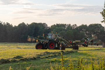 Fototapeta premium Traktor mit Heuwender fährt über eine Wiese