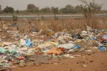 Vue rapprochée d'une décharge sauvage au Sénégal composée de déchets en plastique et d'emballages en carton et située près d'une route. Symbole de la pollution et de la dégradation de l'environnement.