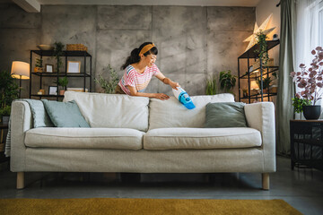 Naklejka premium Mature japanese woman vacuums sofa with a hand vacuum cleaner at home