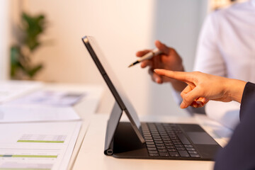 A person is pointing at a laptop screen with a pen in their hand