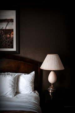 A cozy hotel bedroom setting features a neatly made bed with white pillows and sheets, accompanied by a bedside lamp on a dark nightstand. 