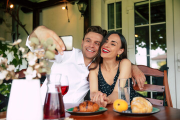 Happy couple taking a selfie at a cozy café with delicious pastries and vibrant drinks in a warm afternoon setting