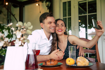 A joyful couple enjoying a cozy brunch together while taking a selfie in a sunlit cafe garden