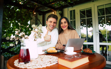 A joyful couple sharing a moment at a cozy café while browsing their phones and enjoying pastries in the bright afternoon light