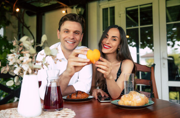 Couple smiling together at a table, holding a heart-shaped dessert during a sunny afternoon in a cozy garden setting