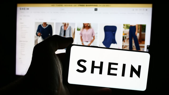 Stuttgart, Germany - 08-16-2024: Person holding mobile phone with logo of fashion e-commerce company Shein in front of business web page. Focus on phone display.
