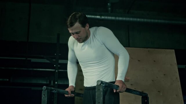 Caucasian young fit man demonstrating straddle planche on bars at loft style sports studio