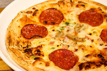 close up of freshly baked pizza or flatbread with salami, cheese, prawns and mayonnaise as toppings on a white plate on a wood table that look crispy and golden