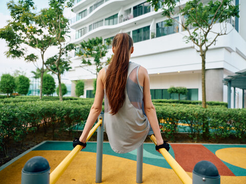 Young woman exercising outdoors on parallel bars in a vibrant park setting