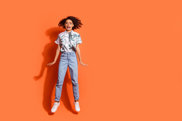 Full body length photo of american woman in jeans and summer stylish shirt jumping trampoline scared isolated on orange color background