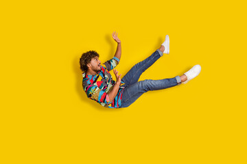 Full size photo of pretty young guy falling down fly wear trendy colorful outfit isolated on yellow...