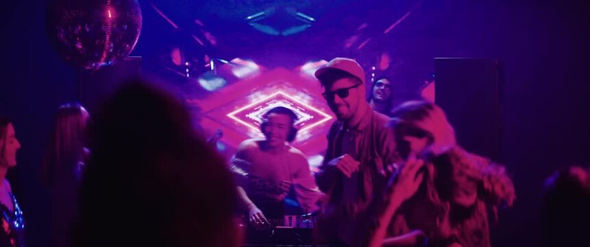 Time-lapse footage of a group of young people dancing and jumping with hands in the air. DJ playing the beats
