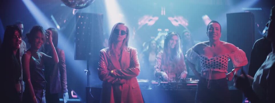 Attractive young woman standing in the middle of the party, looking at the camera while everyone else dancing in the night club
