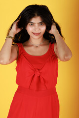 Studio portrait of happy woman in casual clothes. Beautiful confident young Asian Indian girl in red dress standing isolated on yellow background. Fashion concept.