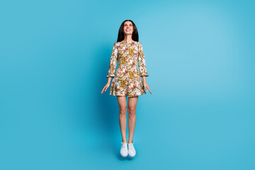 Full length photo of lovely young lady jump look up empty space dressed stylish flowers print garment isolated on blue color background