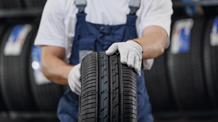 Closeup mechanic holding new tire at store warehouse garage. Replacement of winter and summer tyres