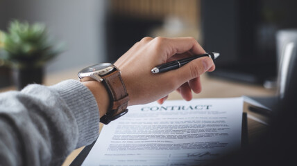 Close-up of a hand with a watch holding a pen over a contract.