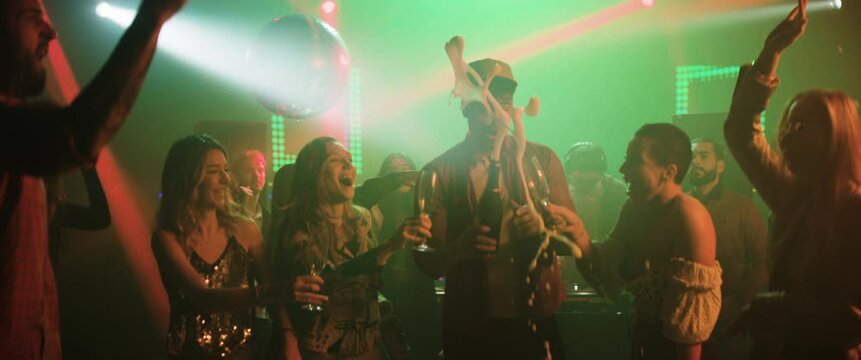 Young people enjoying evening at disco. The man opening beer bottle and everyone else taking beer in glass while dancing