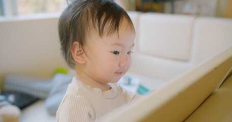 A cute Asian toddler is intently looking at a tablet, showcasing curiosity and concentration. The child is indoors cozy environment emphasize a sense of warmth and comfort.