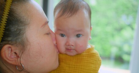 A close-up shot of a mother kissing her baby with a blurred green background, capturing a tender and loving. Tender Moment Between Mother and Baby in Bright Natural Light