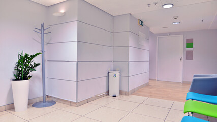 Modern waiting medical office area with white walls, a  tile floor and a row of armchairs.