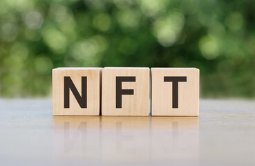 Wooden blocks arranged to spell out the acronym NFT on a table.