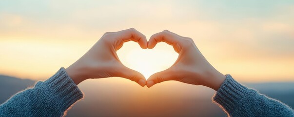 A pair of hands forms a heart shape against a beautiful sunset, symbolizing love and connection in a serene landscape.