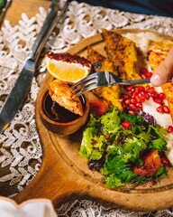 Person enjoying delicious grilled chicken breast with salad on wooden board